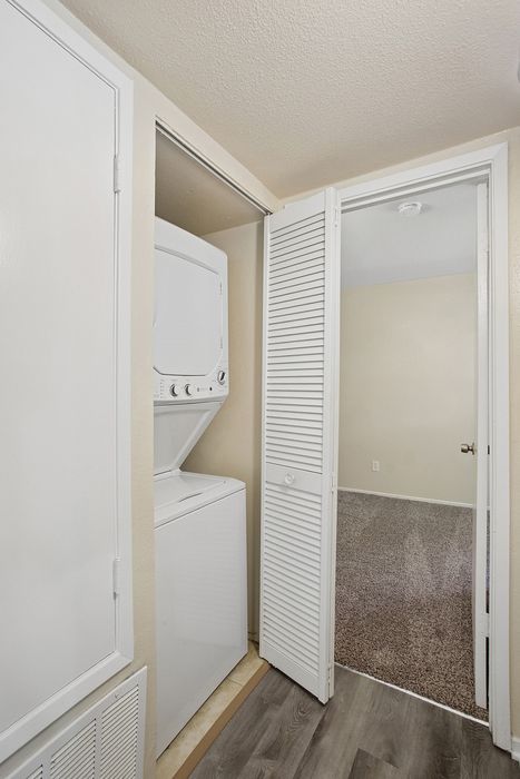 Modern apartment featuring a convenient in-unit laundry setup with a stackable washer and dryer, nestled next to a cozy carpeted room.