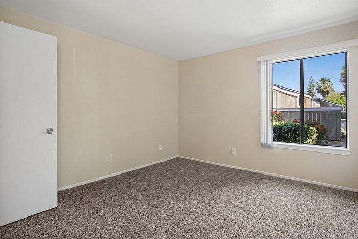 Bright and inviting room with plush carpet and a large window showcasing a vibrant outdoor view, perfect for cozy living.