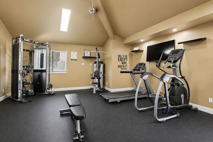 Modern fitness room equipped with state-of-the-art gym machines, including a treadmill and weight bench, set against a stylish beige interior.