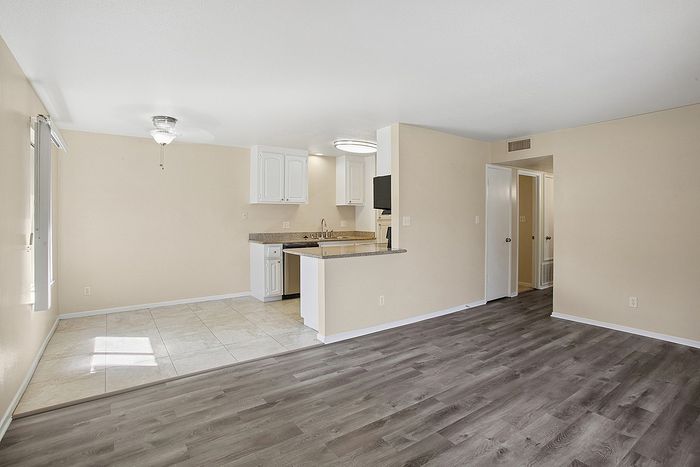 Modern open-plan living space with elegant laminate flooring, a compact yet stylish kitchen featuring white cabinetry and granite countertops, and a bright dining area with polished tile flooring.