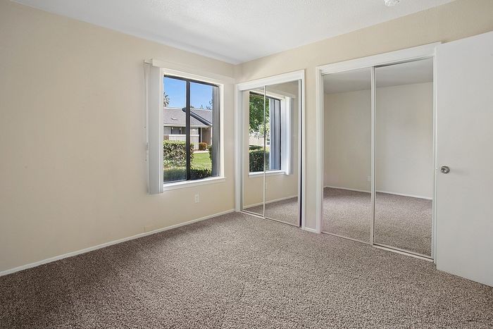 Bright, spacious bedroom with large windows and sleek mirrored closet doors, offering a serene view of a landscaped garden.