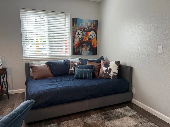 Cozy living space featuring a stylish daybed with plush cushions, modern artwork, and abundant natural light through large window blinds.