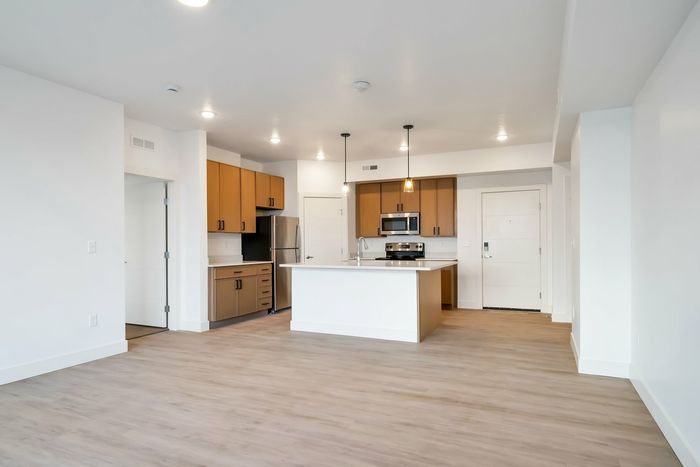 View of the kitchen and main living area. Kitchen has a large island, brown cabinets, and hardwood style flooring.