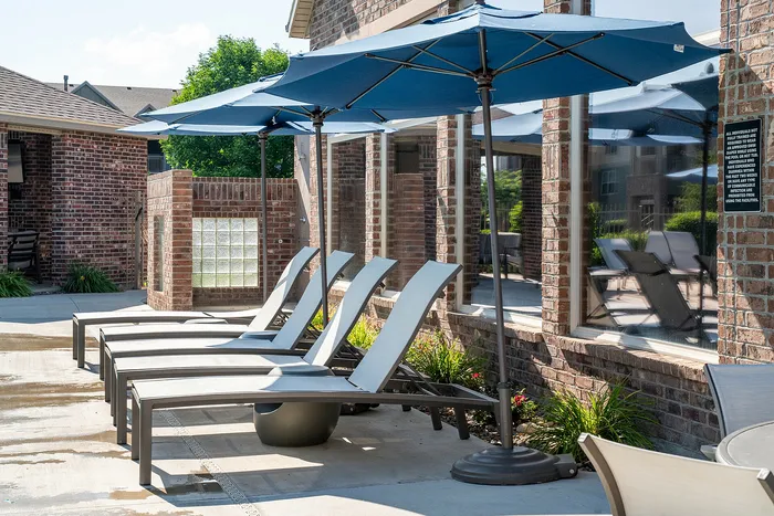 Inviting outdoor lounge area with comfortable reclined chairs and blue umbrellas beside a modern brick building.