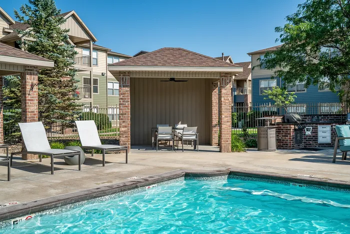Charming outdoor pool area with comfortable loungers, elegant brick cabana, and modern grill station, perfect for relaxation and entertainment.