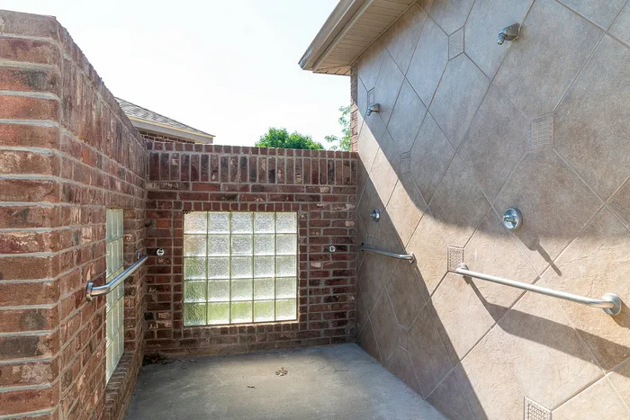 Inviting outdoor shower with elegant brick and tile walls, featuring sleek chrome fixtures and natural light from glass block windows.