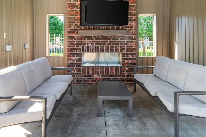 Inviting outdoor seating area with cozy sofas, a stylish brick fireplace, and modern decor. Ideal for relaxation and entertainment.