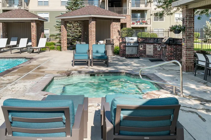 Luxurious outdoor space with inviting pool and spa, comfortable lounge chairs, and a modern barbecue area, set against stylish apartment buildings.
