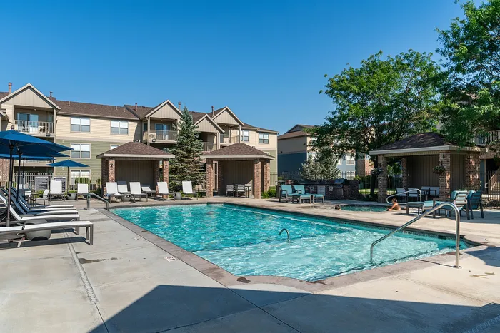 Luxurious apartment complex with a sparkling outdoor pool, sun loungers, shaded cabanas, and lush greenery, perfect for relaxation and enjoyment.