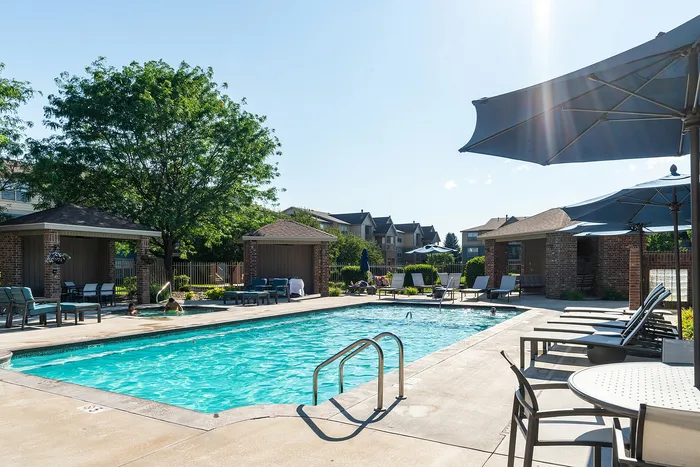 Inviting outdoor pool area with sun loungers and shaded seating, perfect for relaxation and leisure in a serene residential community.