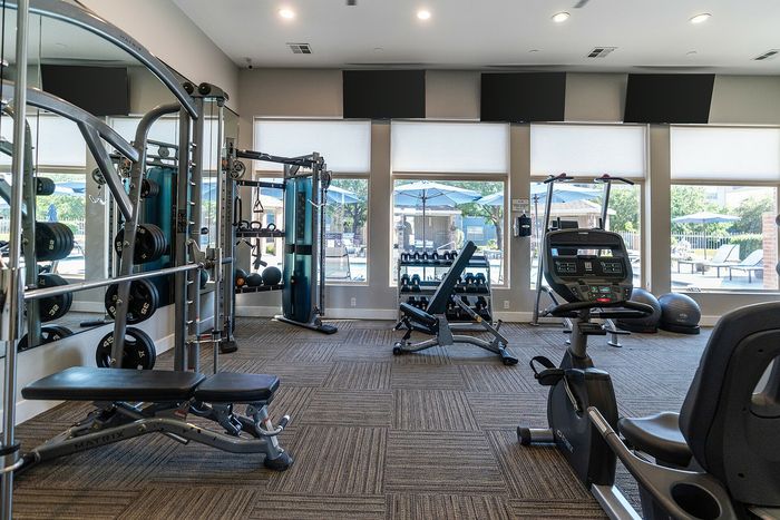 Modern gym with advanced fitness equipment, sunny windows, and poolside views for an invigorating workout experience.