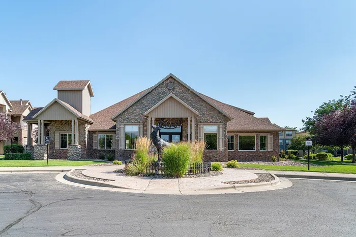 Charming clubhouse exterior with stone facade, landscaped entrance, and a striking sculpture centerpiece.