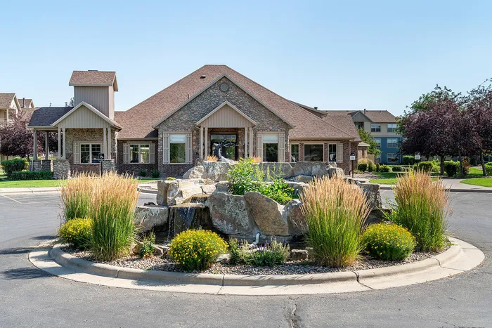 Charming apartment exterior with rustic stonework, surrounded by lush landscaping and a picturesque water feature.