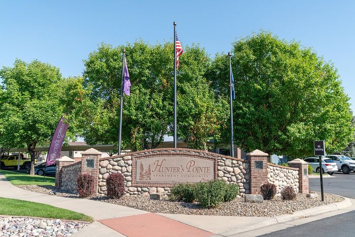 Welcoming entrance to Hunter's Pointe Apartment Community featuring a charming stone sign surrounded by lush green trees and vibrant landscaping.