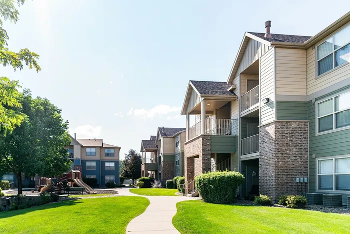 Sunny apartment complex with charming balconies, lush greenery, and playground access.