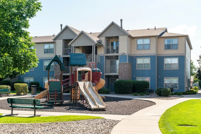 Charming apartment complex with modern design and a vibrant playground, nestled in lush greenery for family-friendly living.