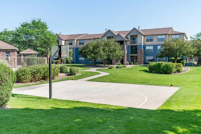 Charming apartment complex with lush green lawns, a basketball court, and mature trees for serene outdoor living.