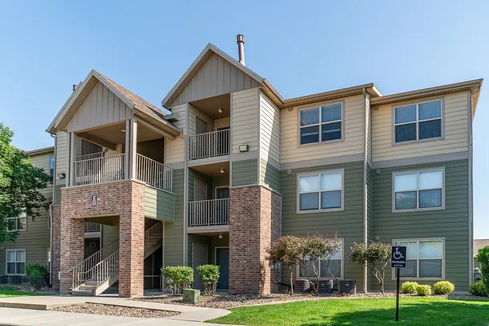 Charming three-story apartment building with inviting balconies, modern brick accents, and lush landscaping on a sunny day.