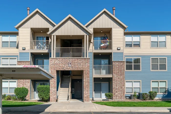 Charming three-story apartment building with modern architecture, private balconies, and elegant brick detailing under a clear blue sky.