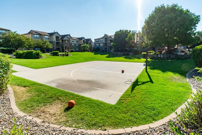 Vibrant apartment community with lush green lawns and a sunlit basketball court, perfect for active outdoor living.