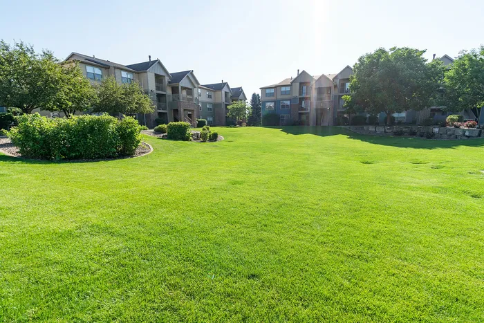 Vibrant apartment community with lush green lawns and modern buildings nestled among mature trees, perfect for relaxed living.
