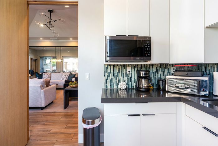Modern kitchen with sleek white cabinetry, stainless steel appliances, and a chic tile backsplash opening to a cozy living room with stylish decor.