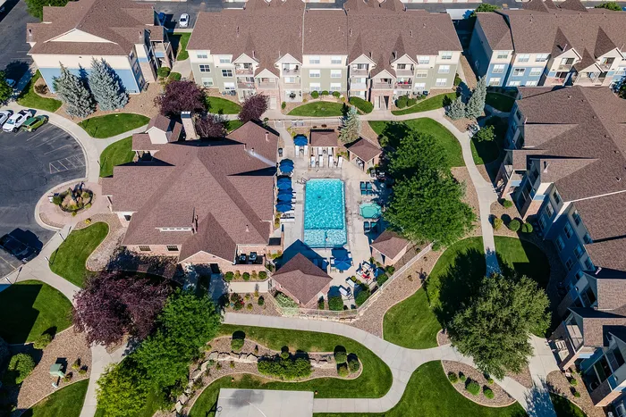 Aerial view of a luxurious apartment complex featuring a sparkling central swimming pool, beautifully landscaped paths, and vibrant green spaces.
