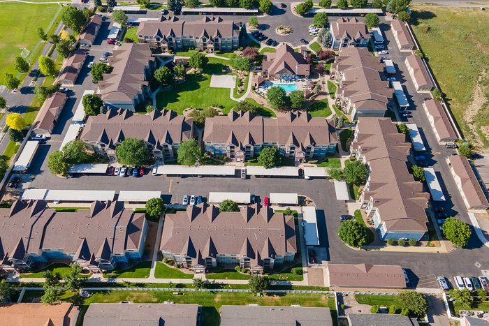 Aerial view of a charming residential complex featuring beautifully landscaped gardens, a central pool, and spacious brown-roofed buildings surrounded by greenery.