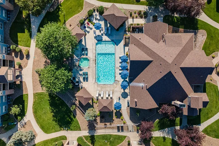 Aerial view of a beautifully landscaped apartment complex featuring a sparkling blue pool, inviting lounge chairs, and vibrant green lawns.