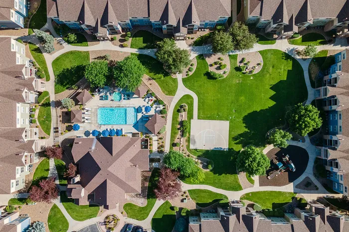 Aerial view of a modern apartment complex featuring lush green spaces, a sparkling swimming pool, a basketball court, and a children's playground.