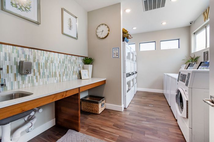 Bright and modern laundry room featuring stacked washers and dryers, elegant backsplash, and ample counter space with stylish decor.