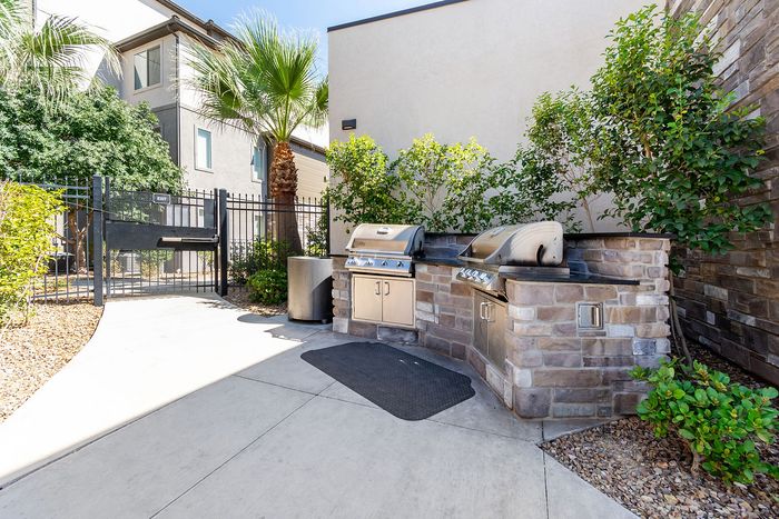 Charming outdoor grill area with stylish stonework, lush greenery, and a gated ambiance perfect for summer BBQs.