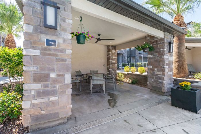 Charming outdoor seating area under covered patio with rustic stone pillars and vibrant hanging plants.