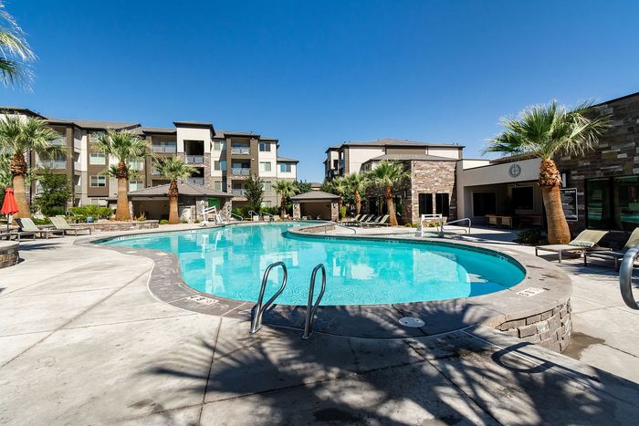 Luxurious apartment community featuring a sparkling swimming pool, surrounded by palm trees and modern architecture.