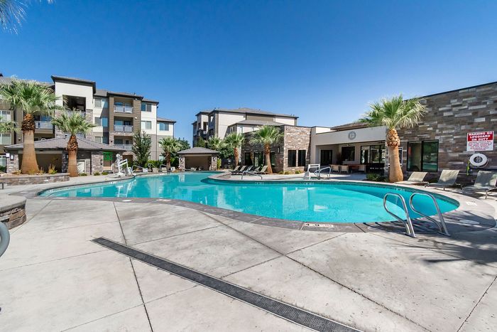 Luxurious apartment complex with a stunning outdoor pool surrounded by palm trees and modern buildings.
