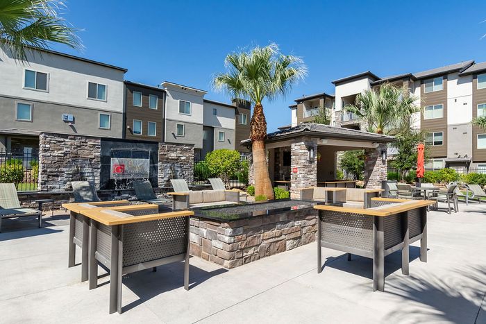 Luxurious apartment community with a stylish outdoor lounge area featuring modern seating, a palm tree, and a stone fireplace.