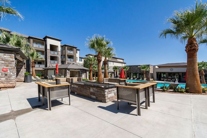 Luxurious apartment complex featuring a sunlit outdoor area with palm trees, modern seating, and a pristine swimming pool, perfect for relaxation.