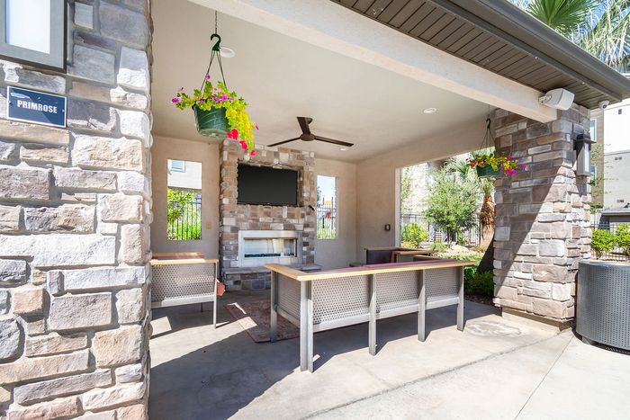 Charming outdoor pavilion featuring a stone fireplace, ceiling fan, and hanging floral baskets, perfect for relaxation or entertaining.