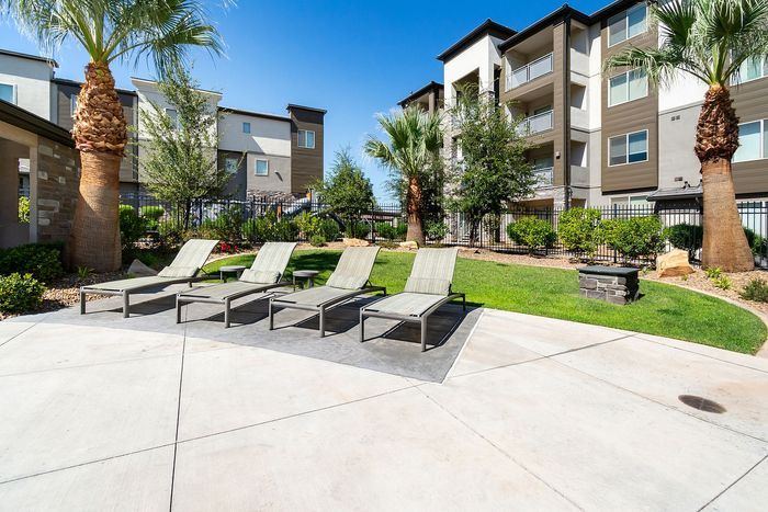 Relaxing outdoor space with sun loungers, lush greenery, and modern apartment buildings.