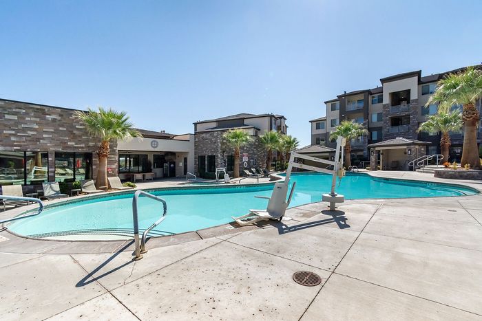 Luxurious apartment complex featuring a pristine pool surrounded by palm trees and modern architecture under a bright blue sky.