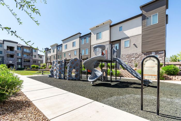 Modern apartment complex with stylish facades, landscaped greenery, and a vibrant children's playground featuring a climbing wall and slide.