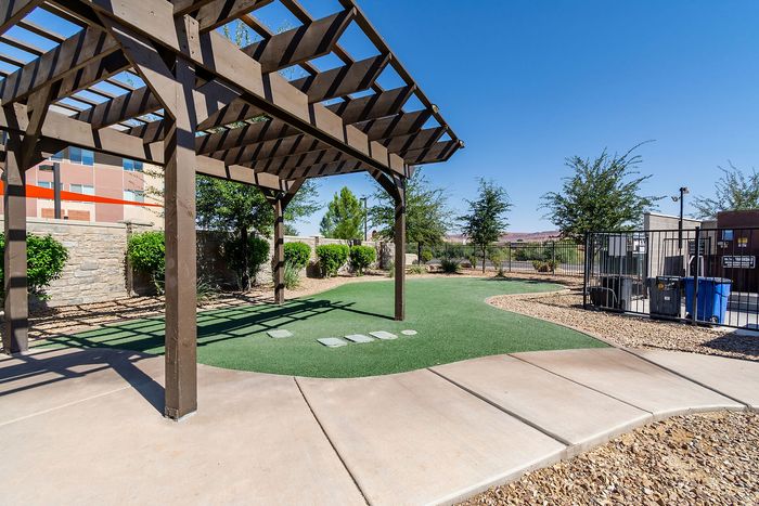 Charming outdoor area with elegant wooden pergola, lush greenery, and manicured pathways under a clear blue sky.