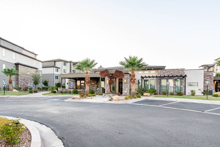 Modern apartment complex exterior with stylish stone and stucco facade, palm trees, and welcoming entrance.