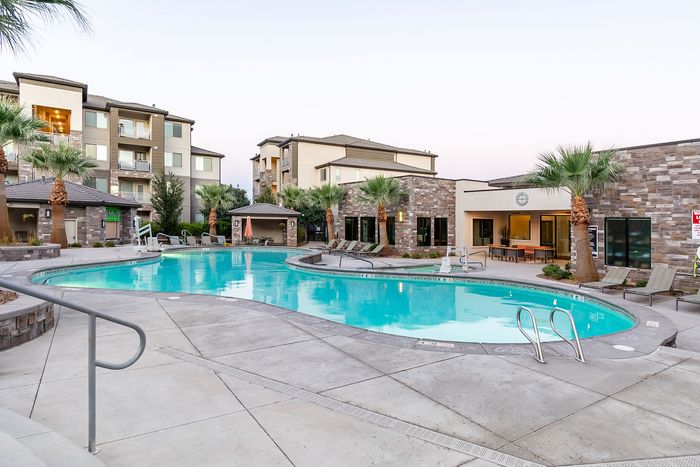 Luxurious apartment community featuring a sparkling swimming pool, surrounded by palm trees and modern stone buildings, promising an oasis of relaxation and comfort.
