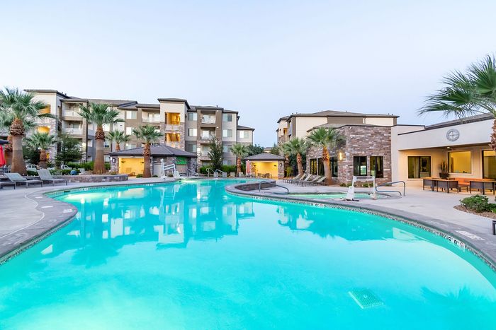 Luxury apartment complex with a stunning outdoor pool surrounded by palm trees and modern architecture.