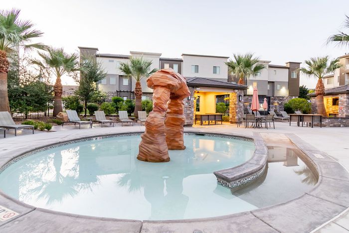 Luxurious apartment complex showcasing a stylish pool area with modern rock sculpture, surrounded by palm trees and elegant lounge chairs.