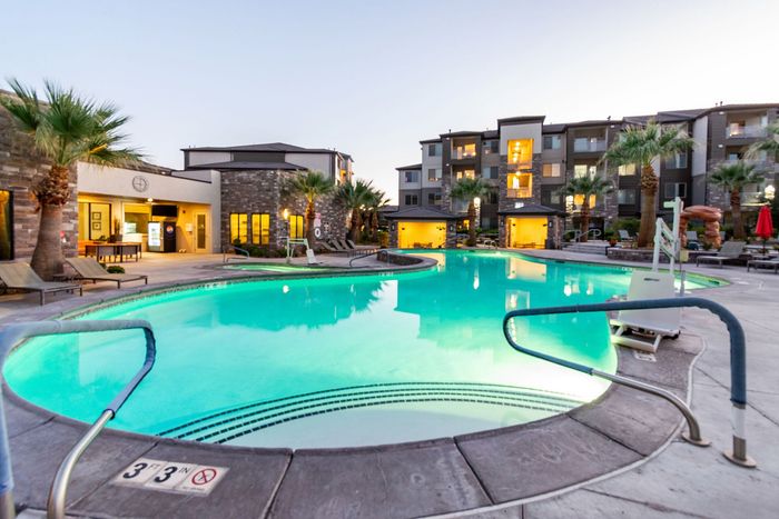 Luxurious apartment complex with a stunning illuminated outdoor pool surrounded by palm trees, offering a relaxing oasis for residents.