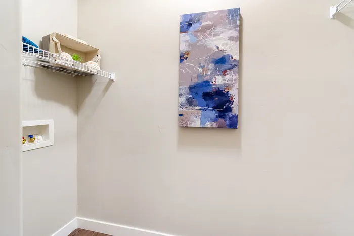 Bright utility room with modern decor, featuring a sleek abstract painting and neatly organized shelf.
