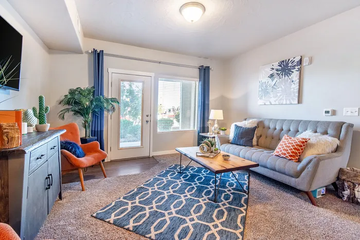 Bright and inviting living room with modern decor, featuring a cozy gray sofa, vibrant orange chair, and stylish geometric rug.