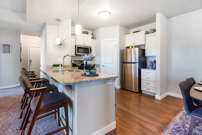 St. George, UT, Townhomes with In-Unit Washer and Dryer - Grayhawk Apartments at River's Edge - White Kitchen With Granite Island, Bar Seating, Stainless Steel Appliances, And Pendant Lights.